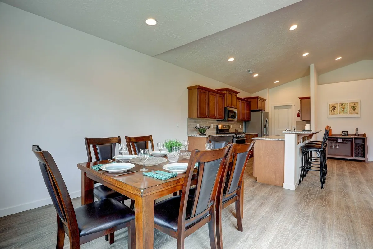 A modern dining table is elegantly set for a meal, adjacent to contemporary kitchen appliances and a bar seating area. The layout invites family dinners, casual gatherings, and effortless entertaining in a warm, welcoming environment.