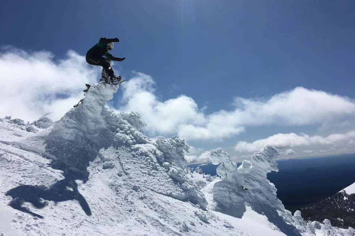 A snowboarder soars mid-air against the dramatic backdrop of a snow-covered peak and distant mountain range, capturing both the thrill of adventure and the region’s beautiful, active landscape.
