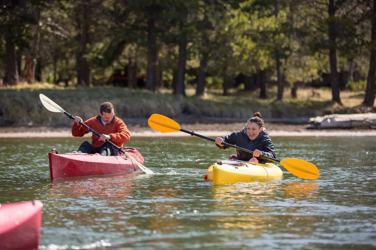 Two brightly colored kayaks glide across a tranquil lake, their occupants enjoying the peaceful water and natural surroundings, with reflections creating a sense of harmony with nature.