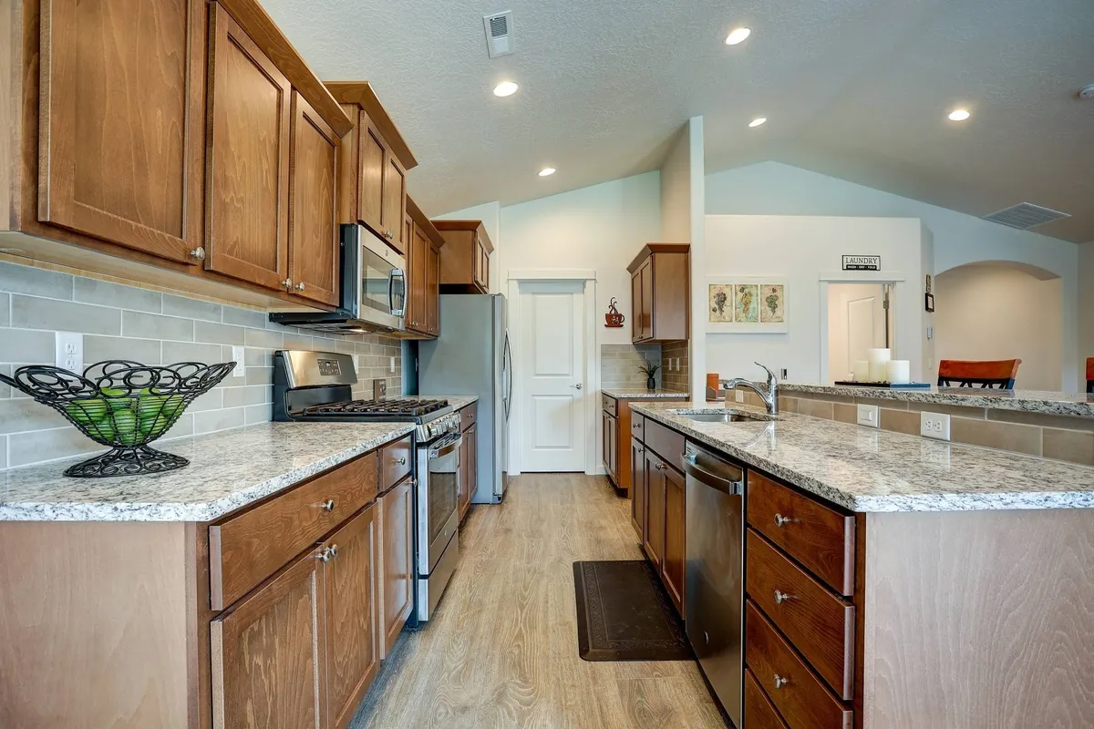 A welcoming kitchen with granite countertops, stainless steel appliances, and warm wood cabinetry. The countertops are clear but include a decorative fruit bowl, making the space look ready for meal prep or gatherings. The kitchen exudes an inviting atmosphere, ideal for fueling up before a day of golf or events.