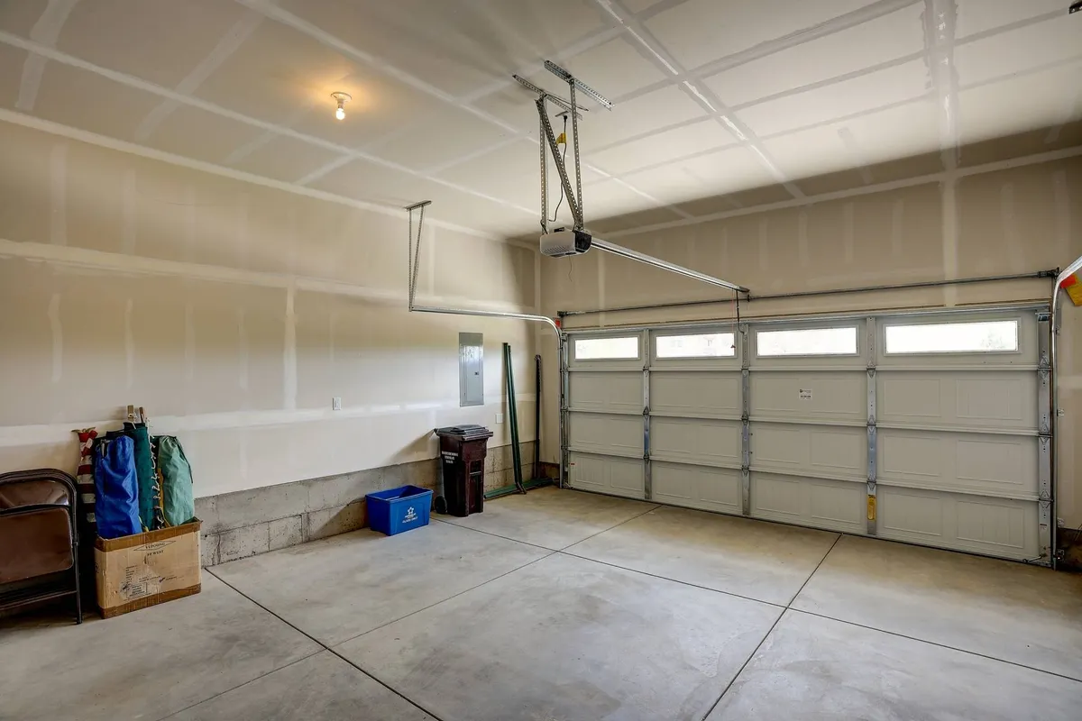 A well-organized garage interior is shown, highlighting a wide garage door, orderly storage, and open floor space suitable for parking vehicles or organizing gear.