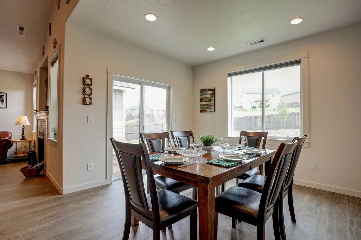 A spacious dining table with chairs sits beside a window offering an inviting view, complemented by decorative wall items, suggesting a warm environment for family meals and gatherings.