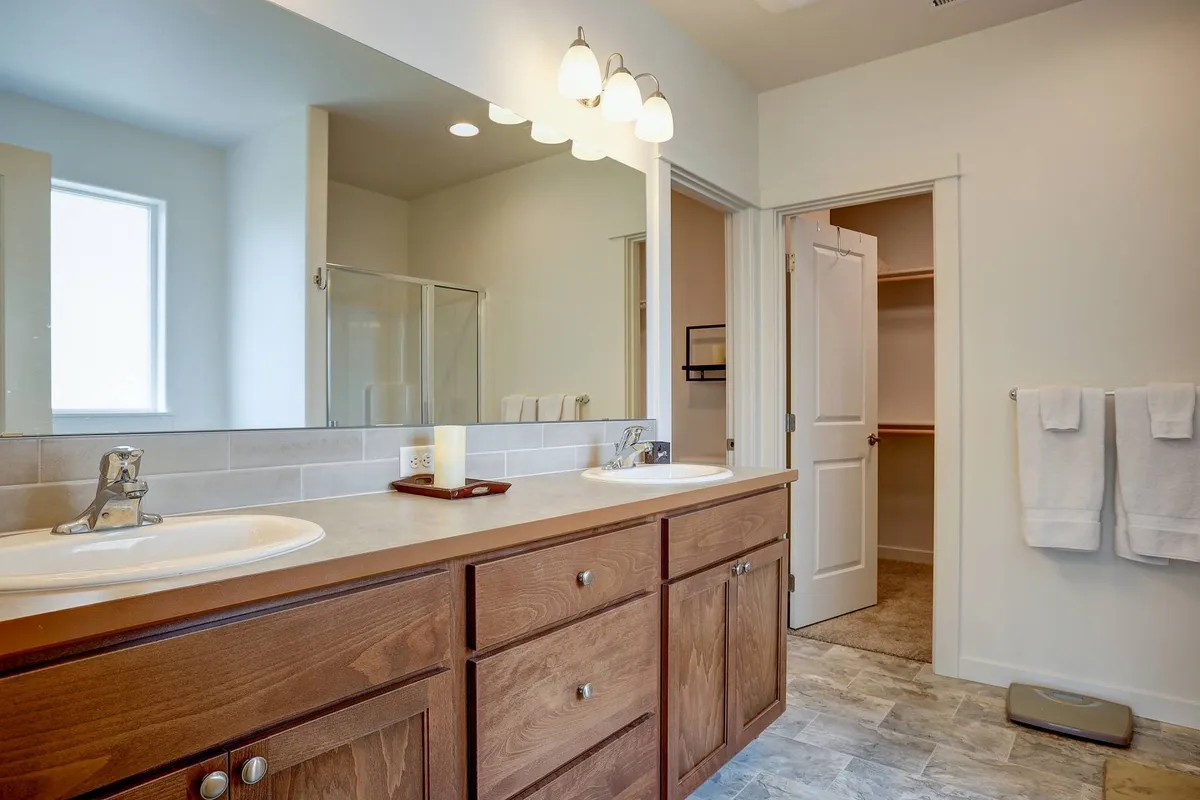 A spacious bathroom featuring a double sink vanity with large mirrors, a modern walk-in shower, and elegant light fixtures. The organized layout and soothing color scheme invite relaxation and rejuvenation.