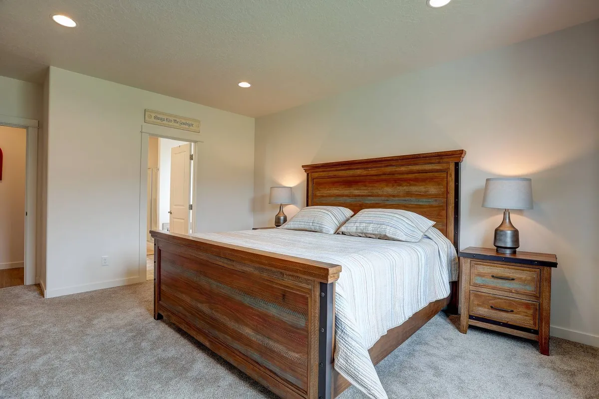 A tranquil bedroom with a wooden bed frame, striped bedding, and bedside lamps. The room’s soft lighting and calm décor evoke a quiet, peaceful ambiance, perfect for relaxation or reading before sleep.