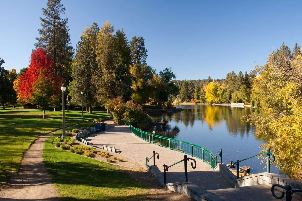 A picturesque lake bordered by colorful trees and a gentle walking path, with inviting park benches overlooking the water—an ideal spot for relaxation or picnicking after a day of adventure.
